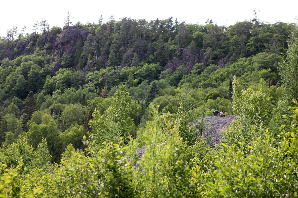 People can be seen looking for rocks on a rock pile in front of the cliff ridge.