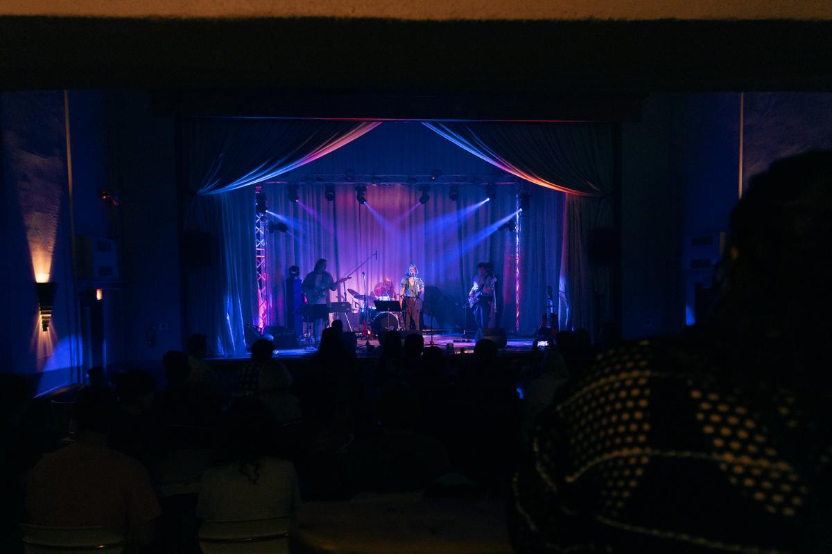 a band plays center on a bright stage surrounded by a moodily lit theater