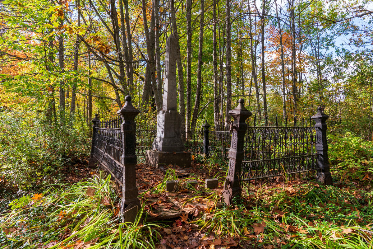 Tombstone surrounded by iron fence in wooded cemetary.