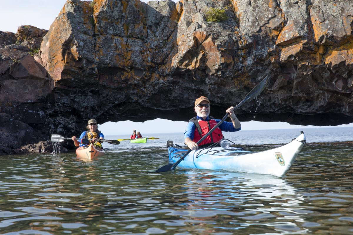 Kayakers paddling under a rock arch in lake superior