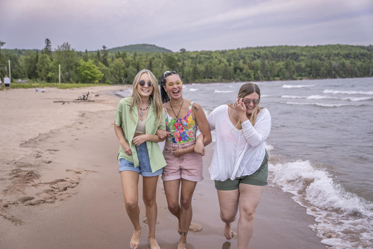 Three girls walk along beach shoreline.