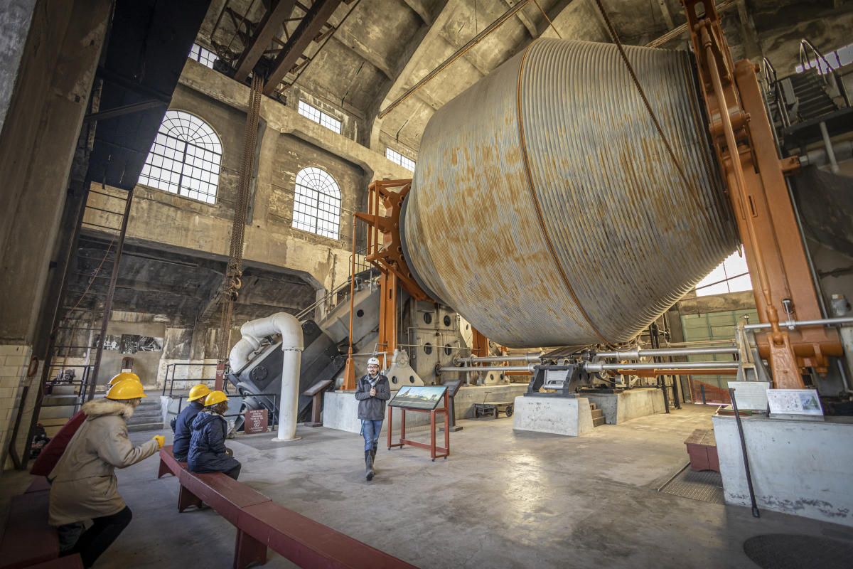 Visitors sit on benches and listen as tour guide provides information about steam hoist.