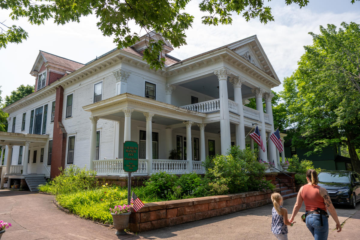a parent holds a child's hand as the walk up to the grand entrance of an antebellum style mansion