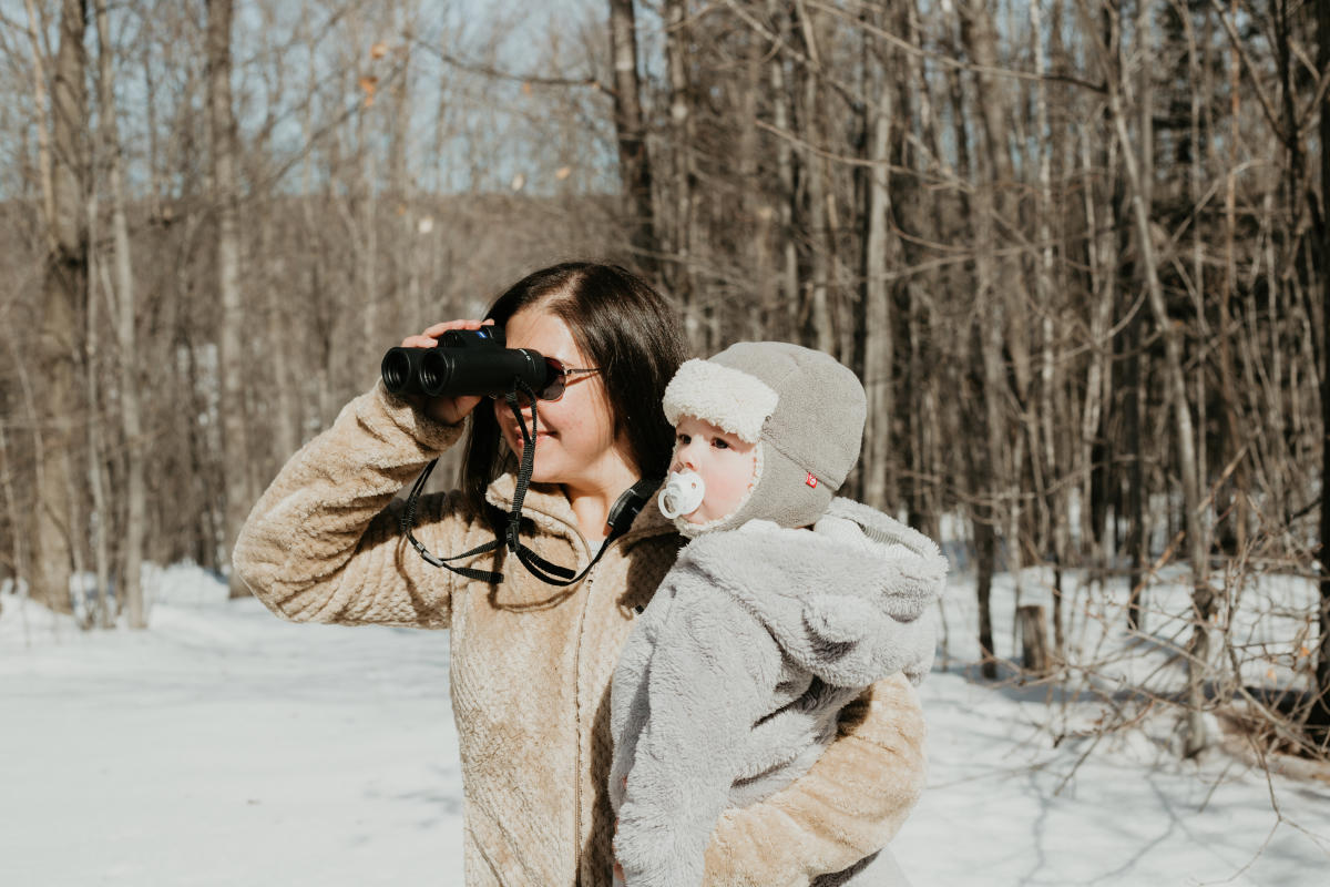 Woman holding baby looks through binoculars.