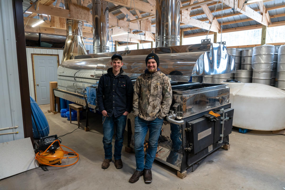 Two men stand in front of giant chrome evaporator.