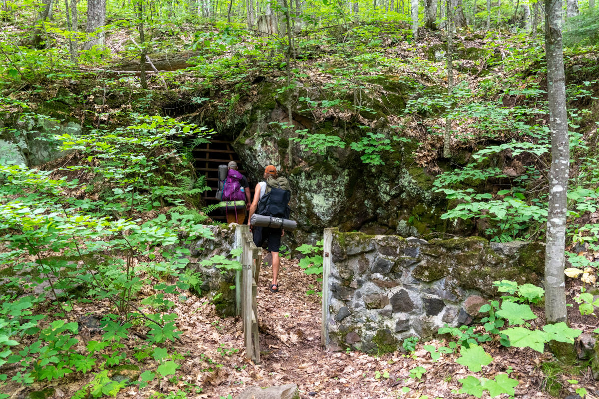 hikers peer into the barred mineshaft entrance