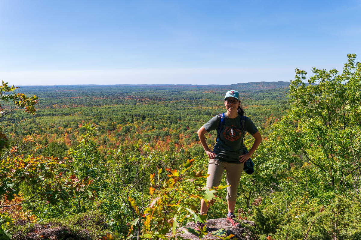 a hiker poses on a cliff's edge overlooking the fall forest