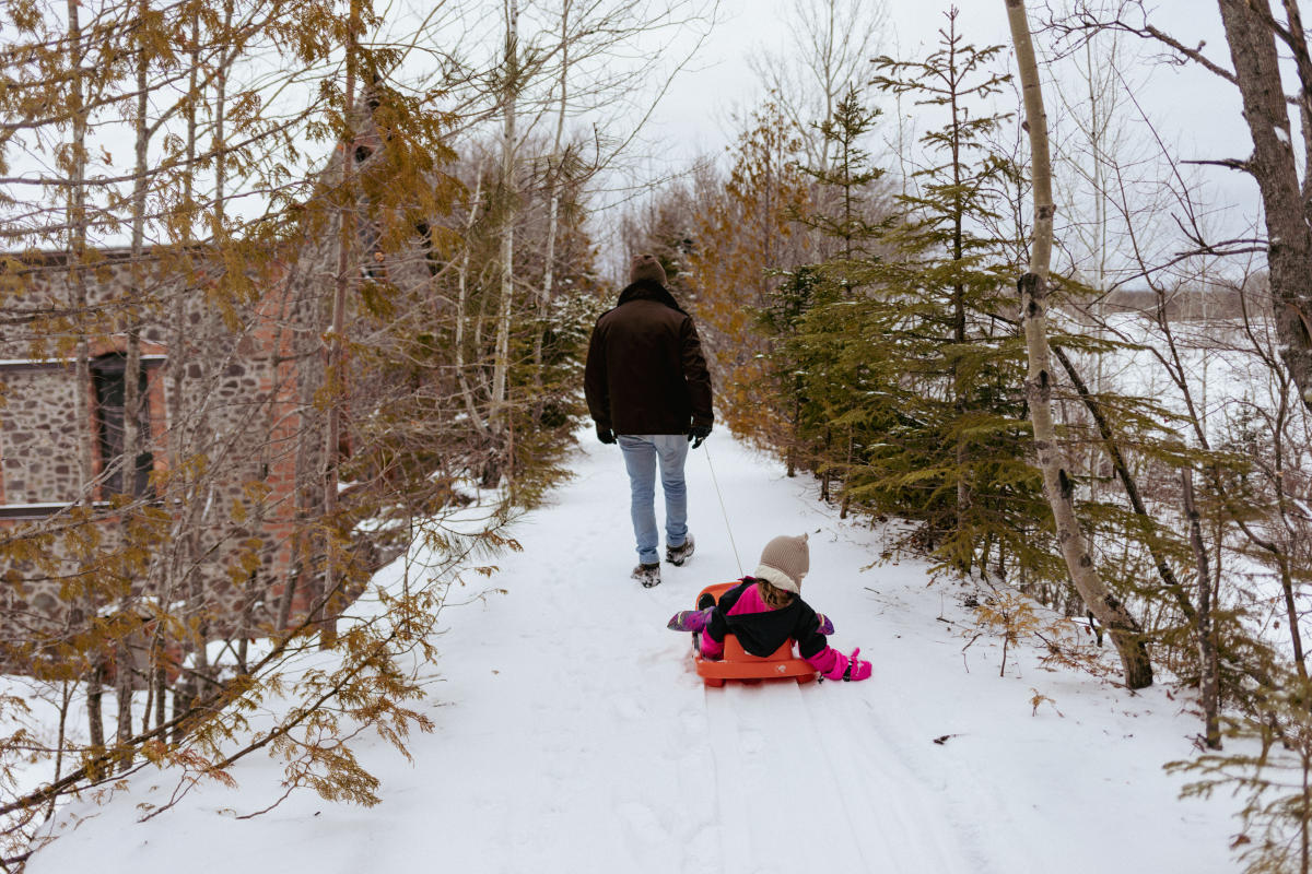 an adult pulls a child on a sled near a historic stone building