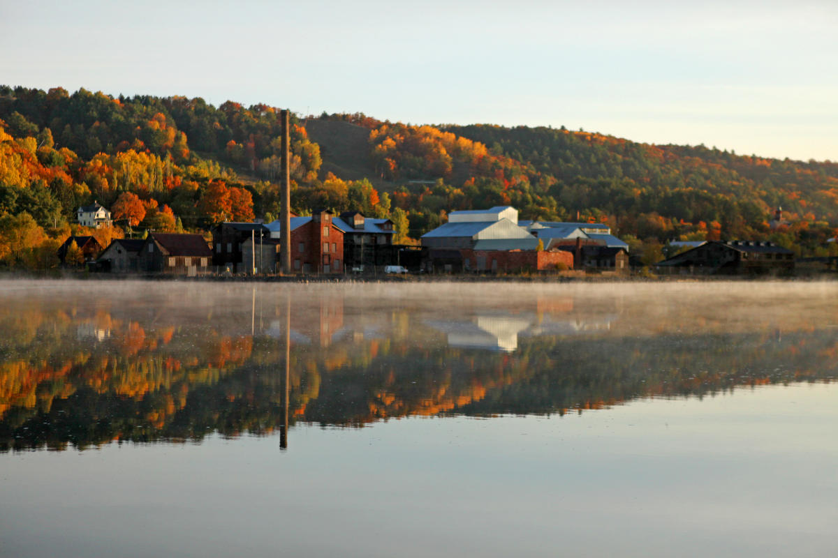Quincy Smelter on glass calm morning with reflections in the canal and fall foliage in background.