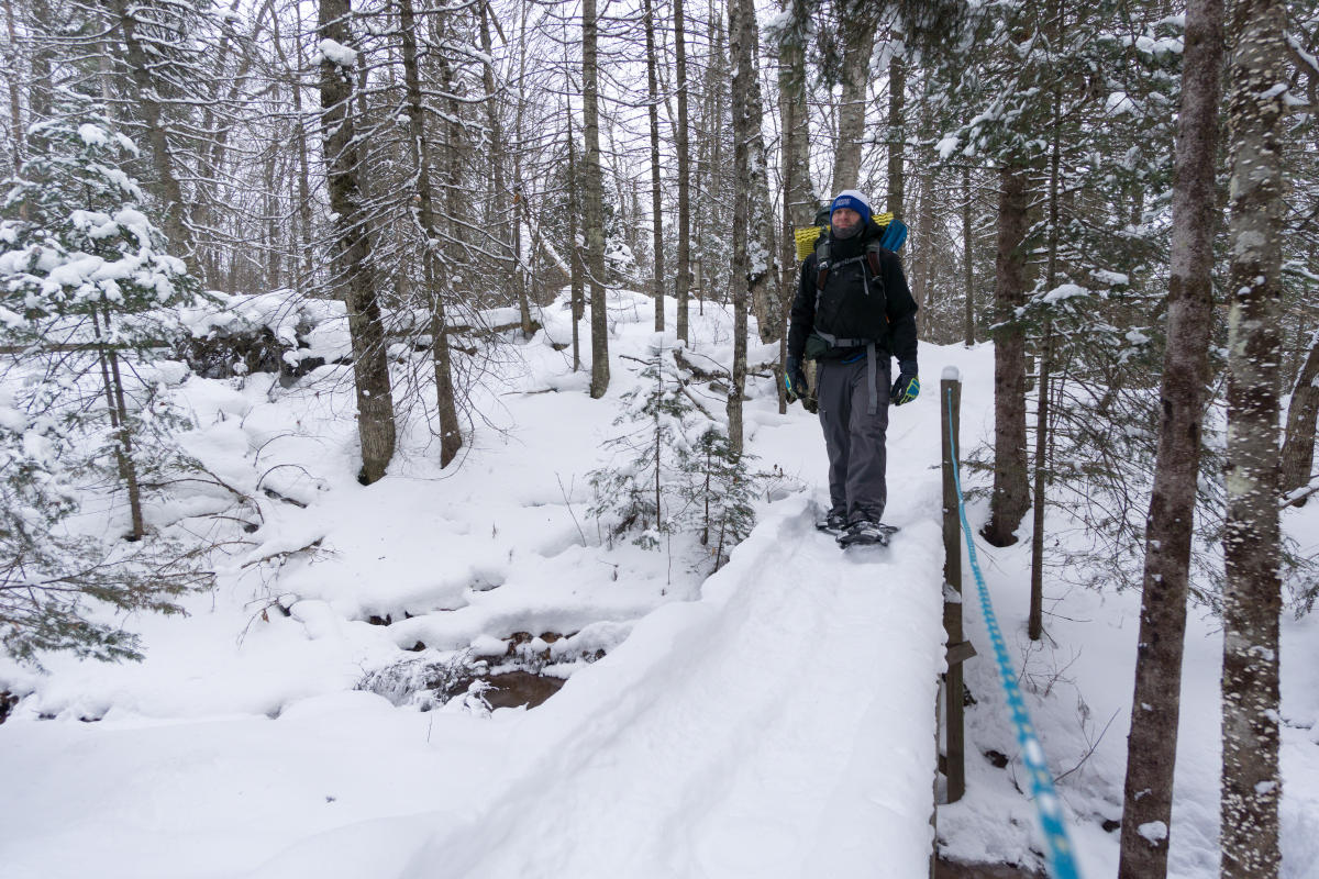 Snowshoer crosses bridge at Tibbets Falls