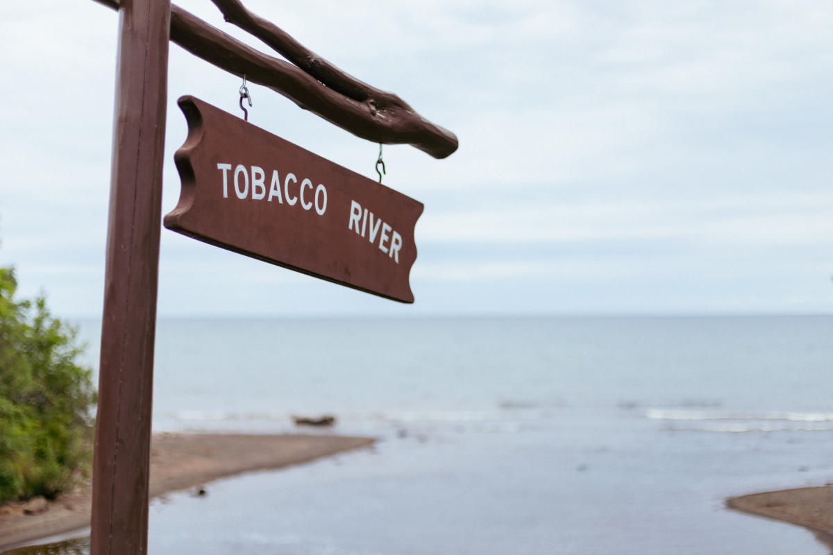 a wooden sign reads Tobacco River with the river's mouth in the background