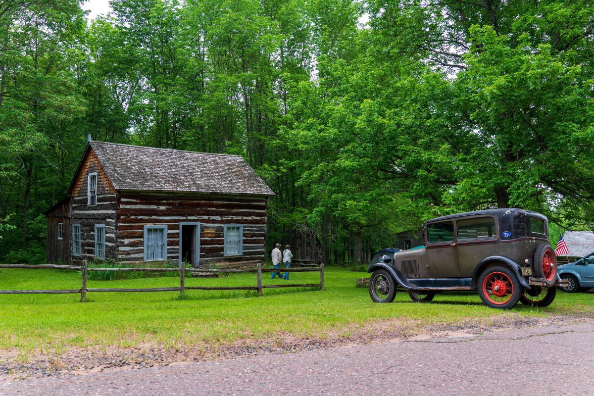 Old Victoria Cabin and old car parked in front.