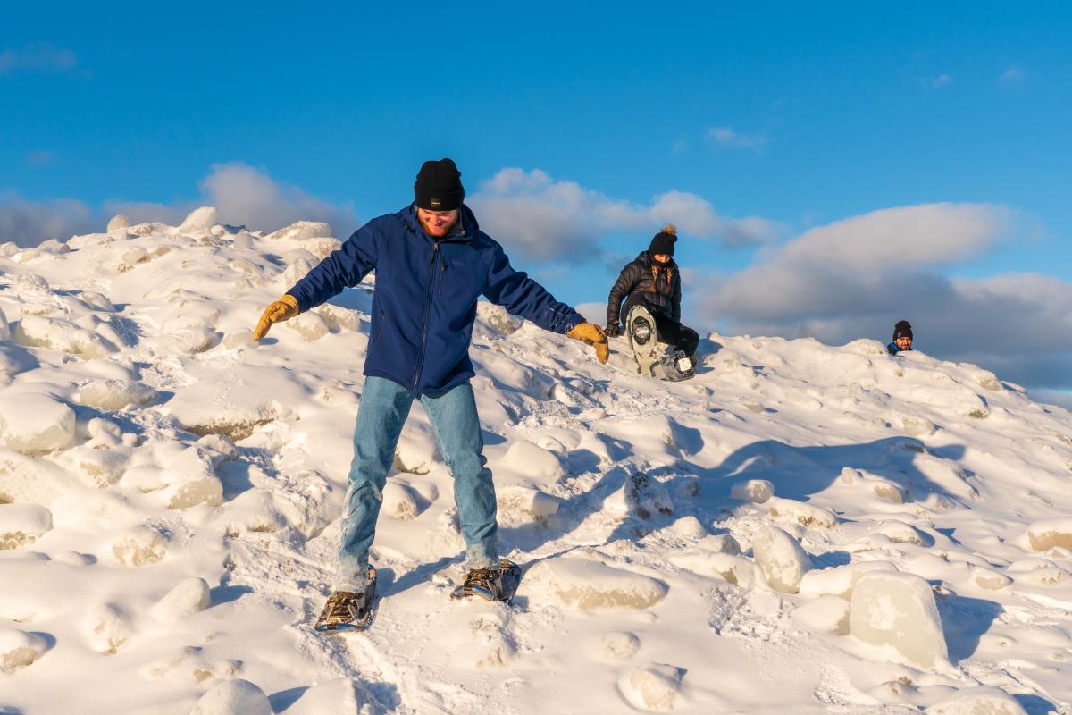 Snowshoers carefully traverse frozen Lake Superior shoreline.