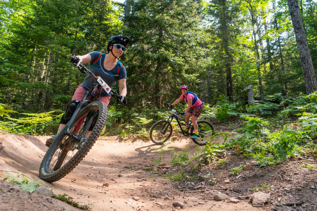 two mountain bikers ride around a forested trail curve