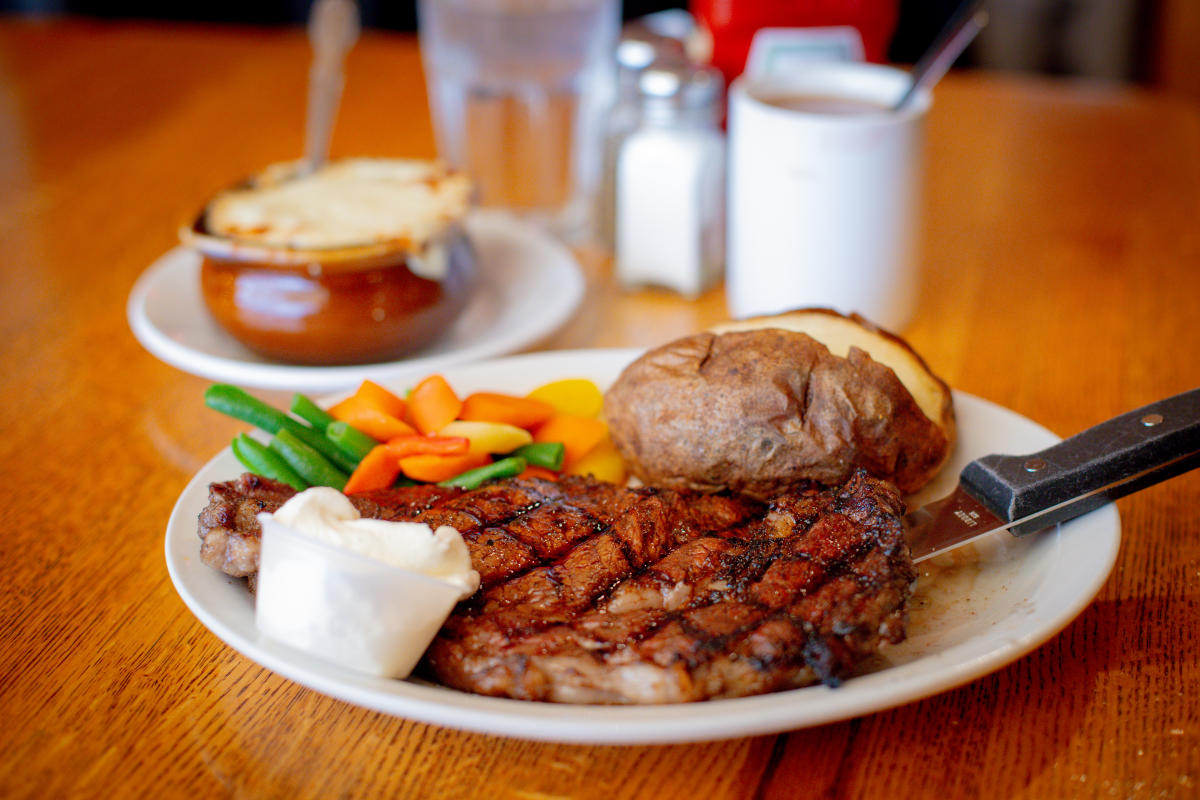 a plate of steak with sides with a bowl of soup in the background