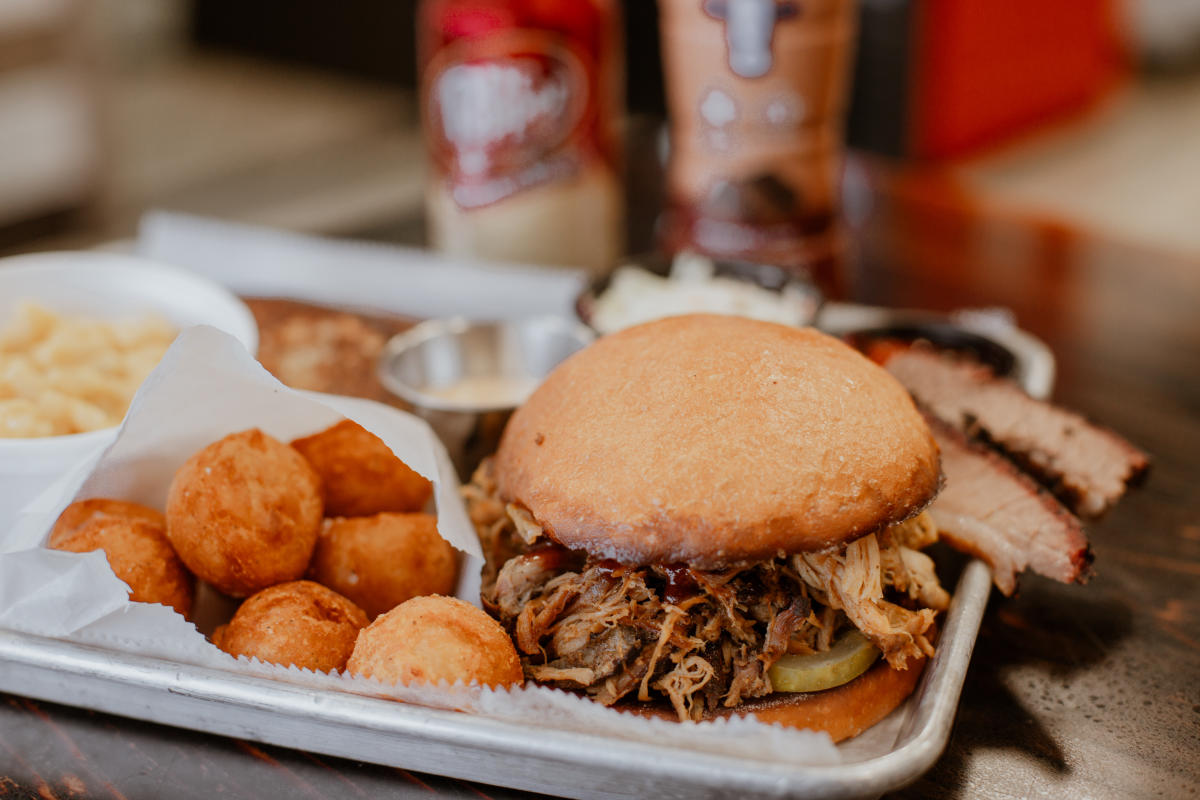 a tray with a pulled pork sandwich and brisket slices with sides