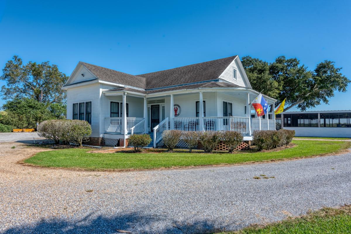 Charming white farmhouse with a porch, featuring flags and neatly trimmed bushes on a sunny day.