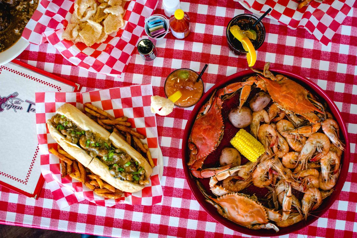 Cooked crab and shrimp in a bowl, next to a shrimp po'boy sandwich.