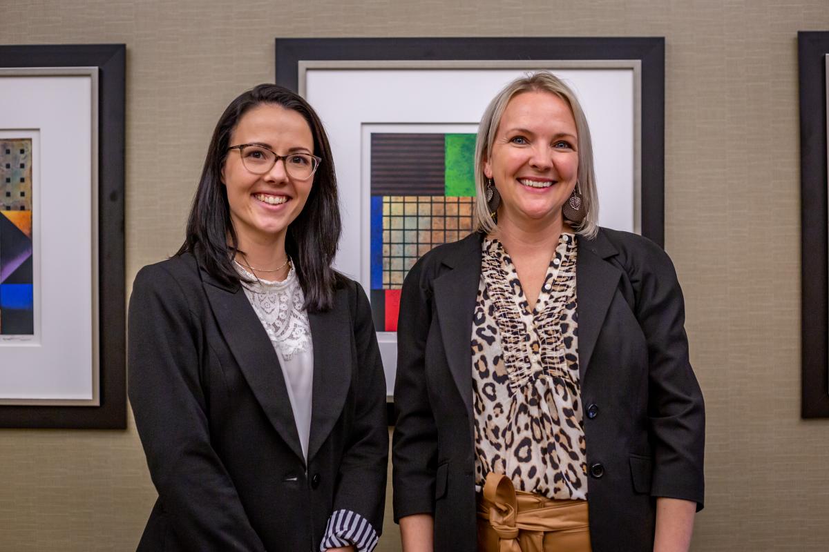 Two women stand next to each other smiling toward the camera.