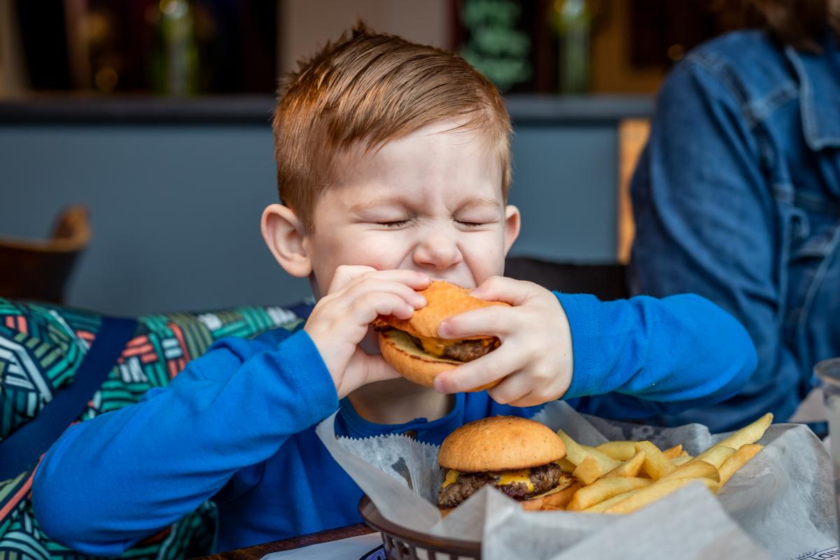 Excited kid taking a bite of a tasty cheeseburger during a fun family outing
