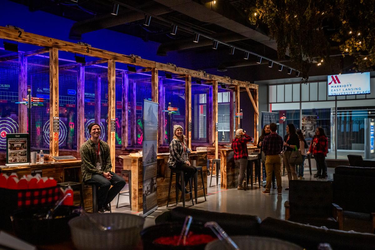 People sitting on stools in High Caliber's axe throwing stalls.