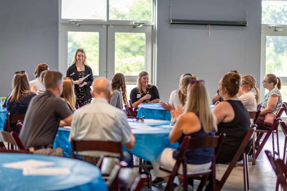 Numerous people meeting indoors seated at multiple tables