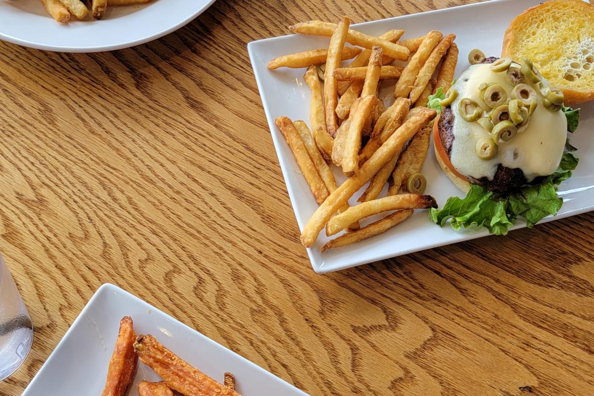 Three white plates with fries and sandwiches on wooden table