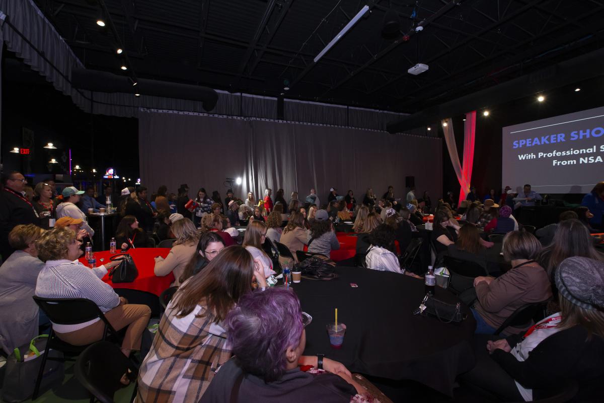 A crowd of people listen to a speaker at High Caliber Karting.