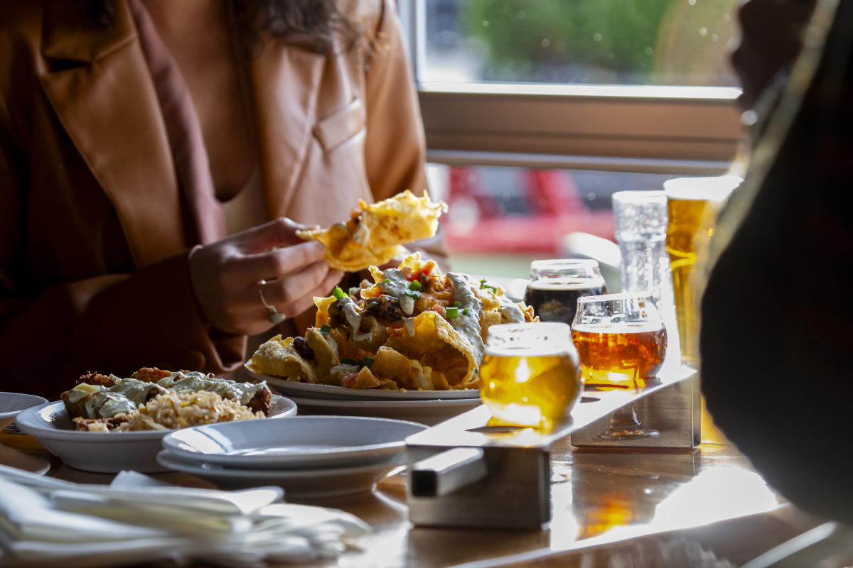 A table eating a big plate of nachos with a flight of beer