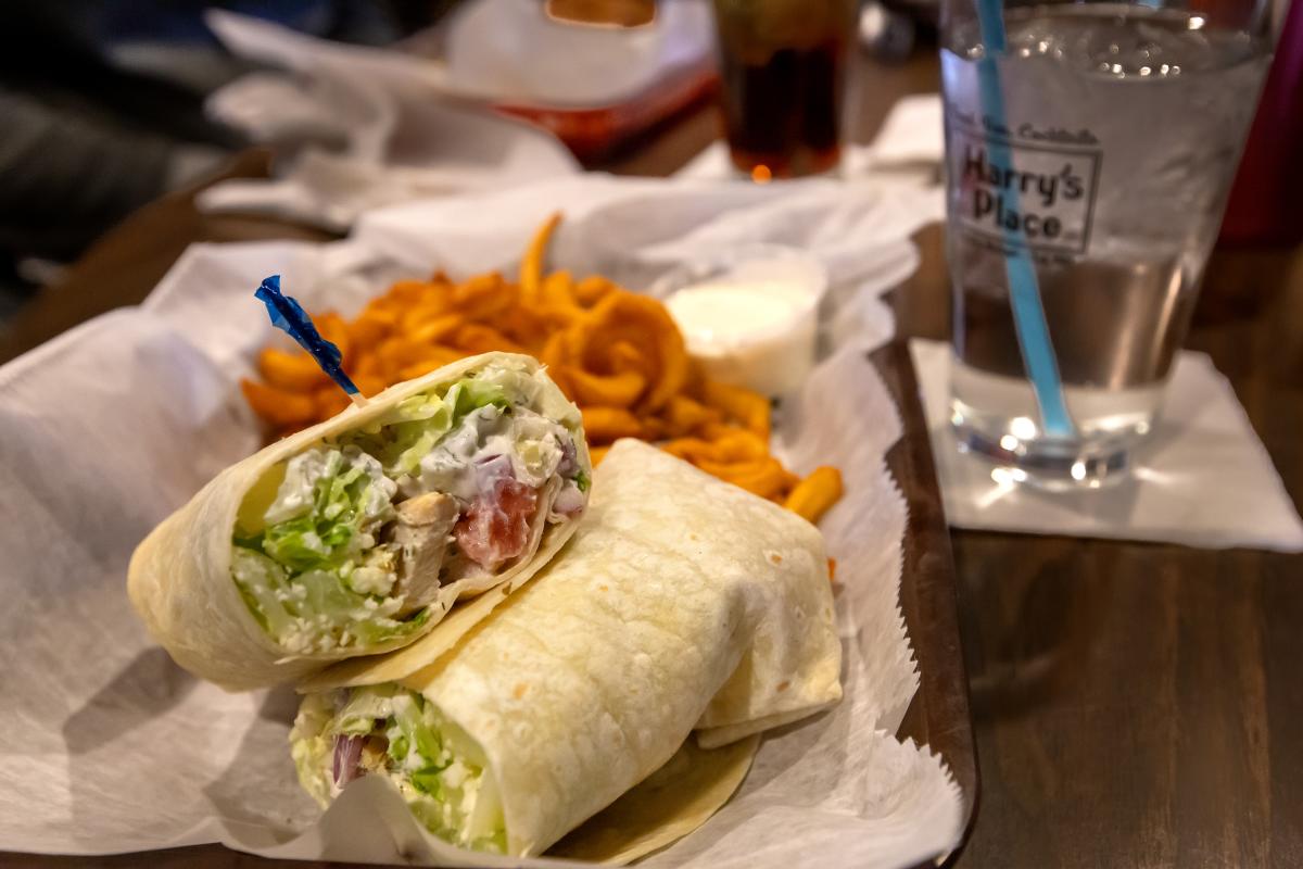 A sandwich wrap on a plate with curly fries and a glass of water