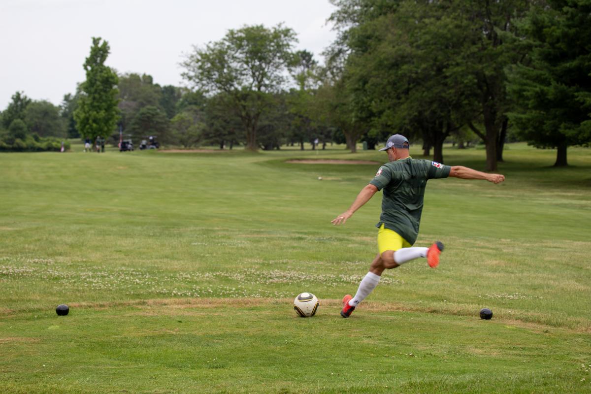 A footgolfer about to kick a ball on green turf.