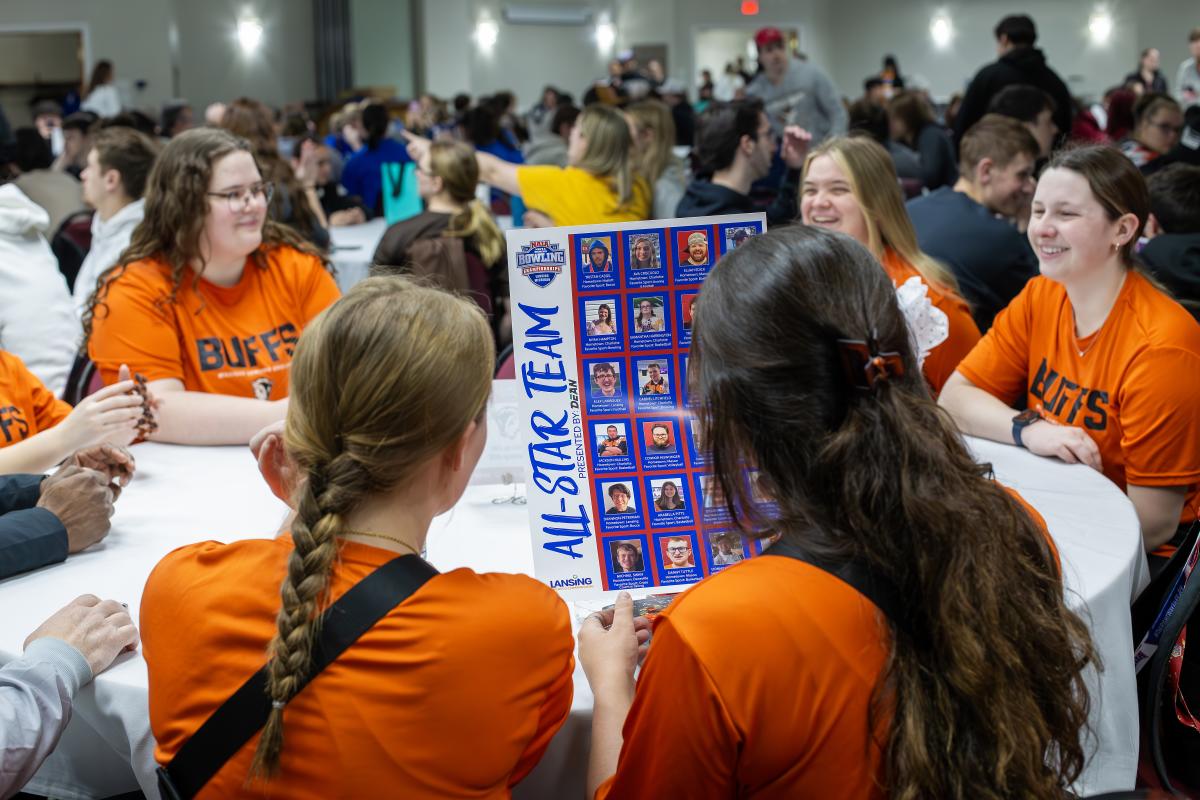 Group of college students sitting at a large round table in a conference room studying the All-Star Team roster