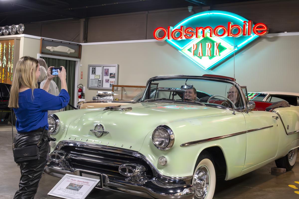 Couple sits inside old convertible while another person takes their photo