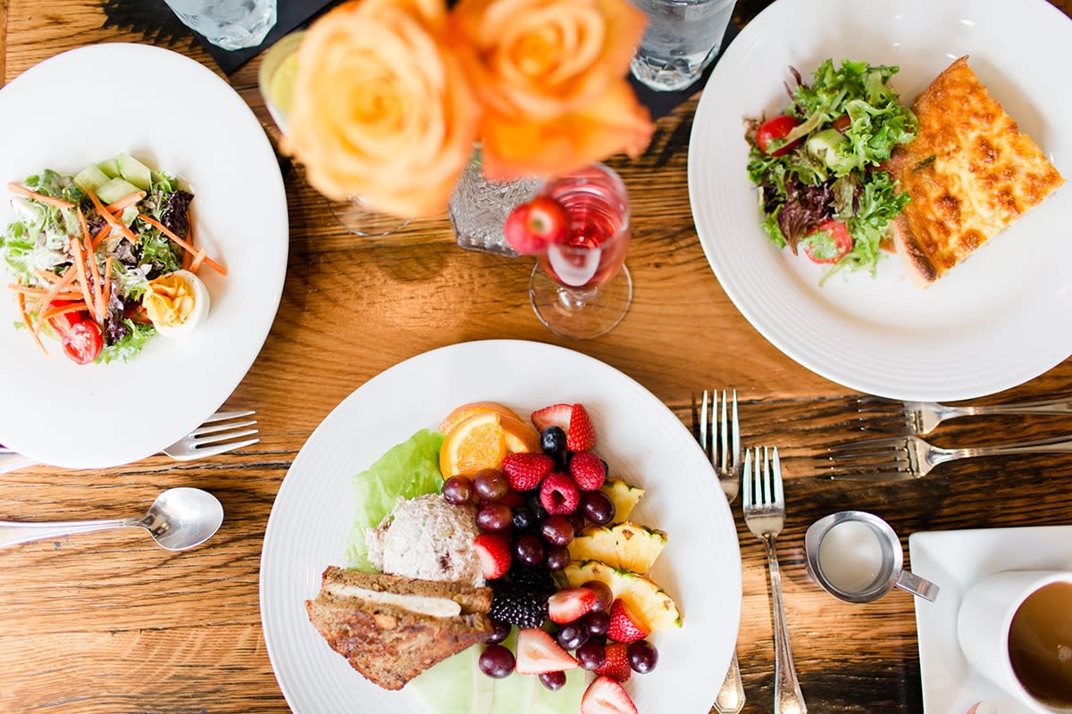 Top down view of three plates of freshly made salad, fruit, and sandwiches on a wooden table.