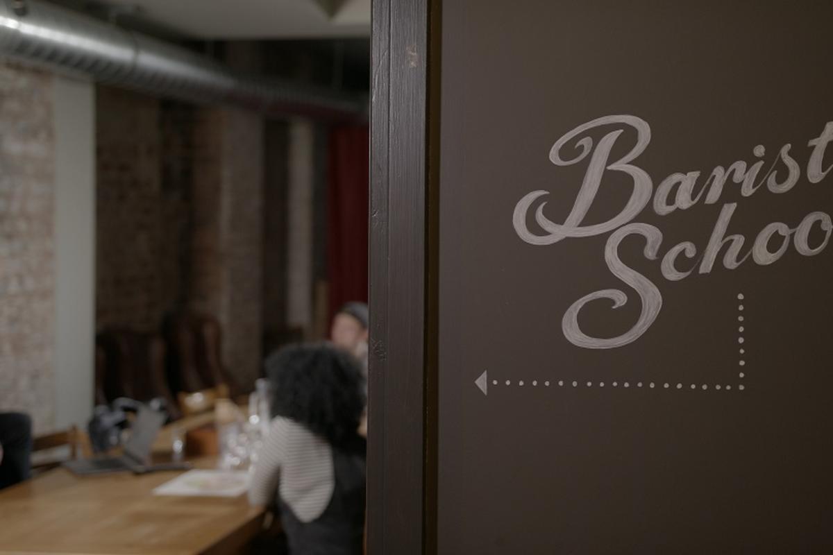 a sign pointing to Barista School where people can be seen at work