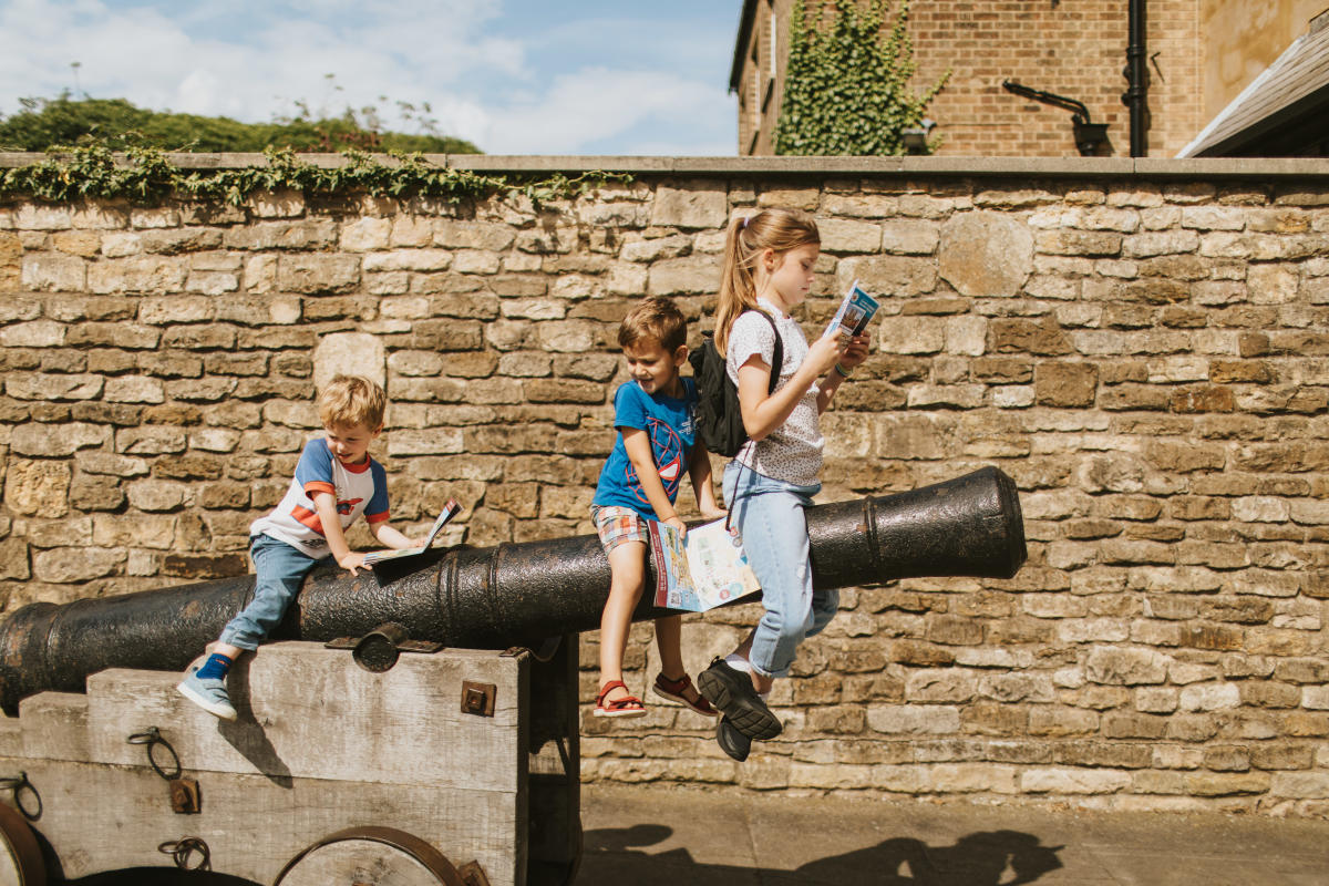 Three children sat on a castle cannon examining a guidebook