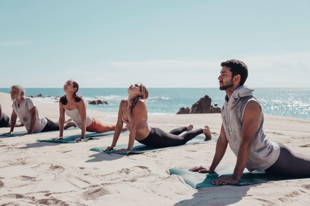 4 personas haciendo yoga en la playa al aire libre de los cabos