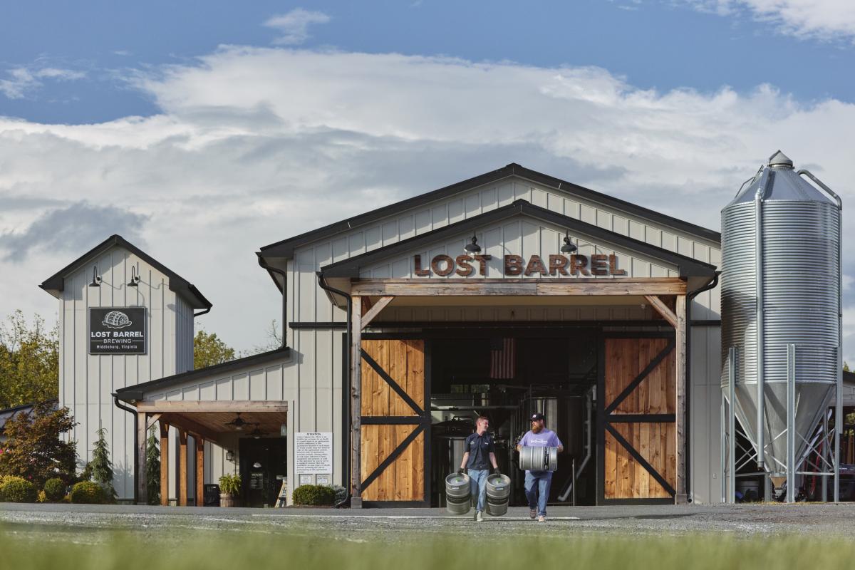 Two staff carrying kegs outside the barn-style entrance of Lost Barrel Brewing in Middleburg, Loudoun