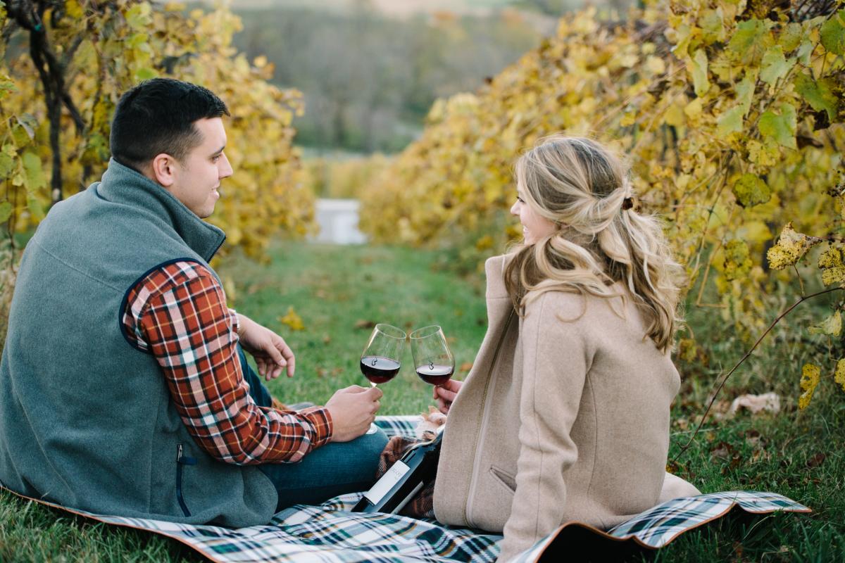 Couple drinking wine while sitting on the ground between in the vines of Bluemont Vineyard