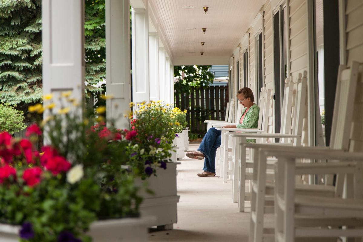 A woman sits on a Mackinac Island porch and reads a book with colorful flowers in the foreground