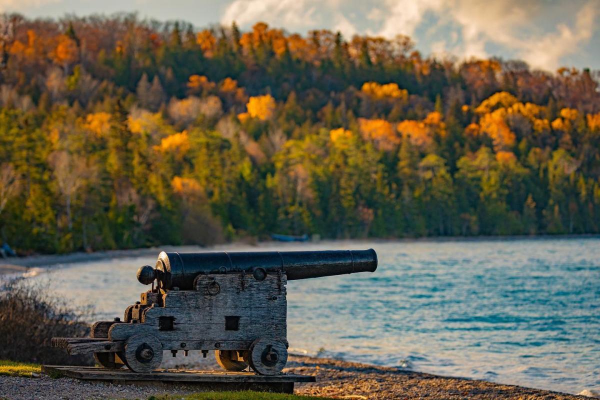 A cannon points out over the water at Mackinac Island’s British Landing, with fall colors on trees in the background