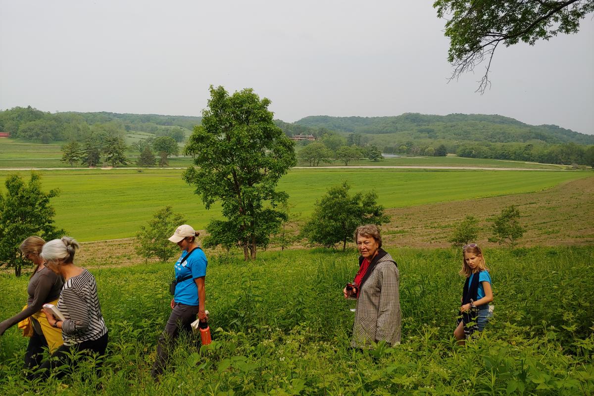 Women walk along a trail with lush green fields in the backdrop