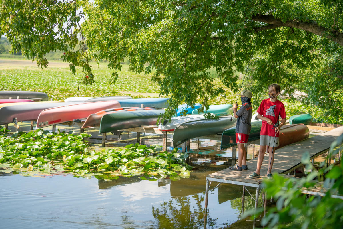 Two kids fishing off a pier next to canoe racks