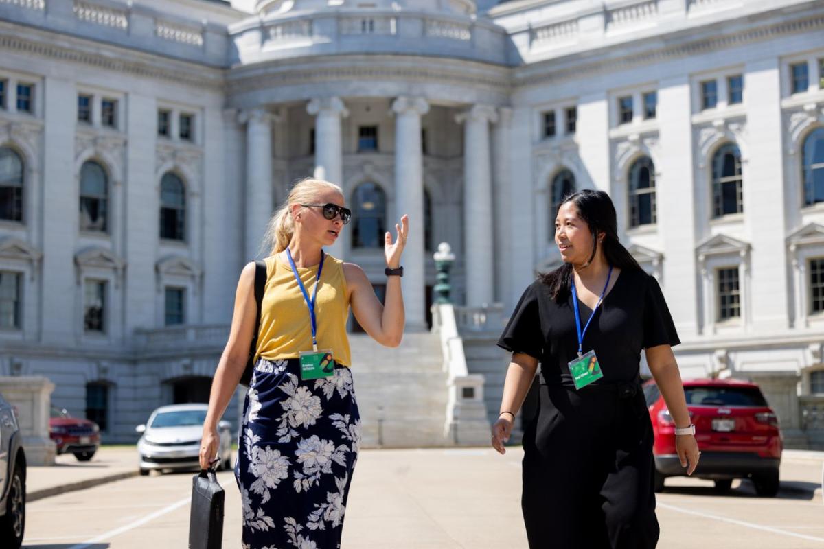 Two women walk in front of the Capitol Building wearing business professional clothing and nametag lanyards from a conference