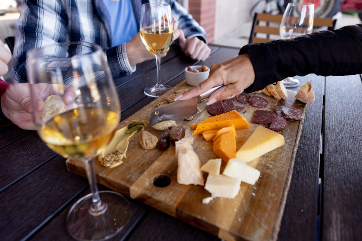 People grab for cheese on a cheese board surrounded by glasses of cider
