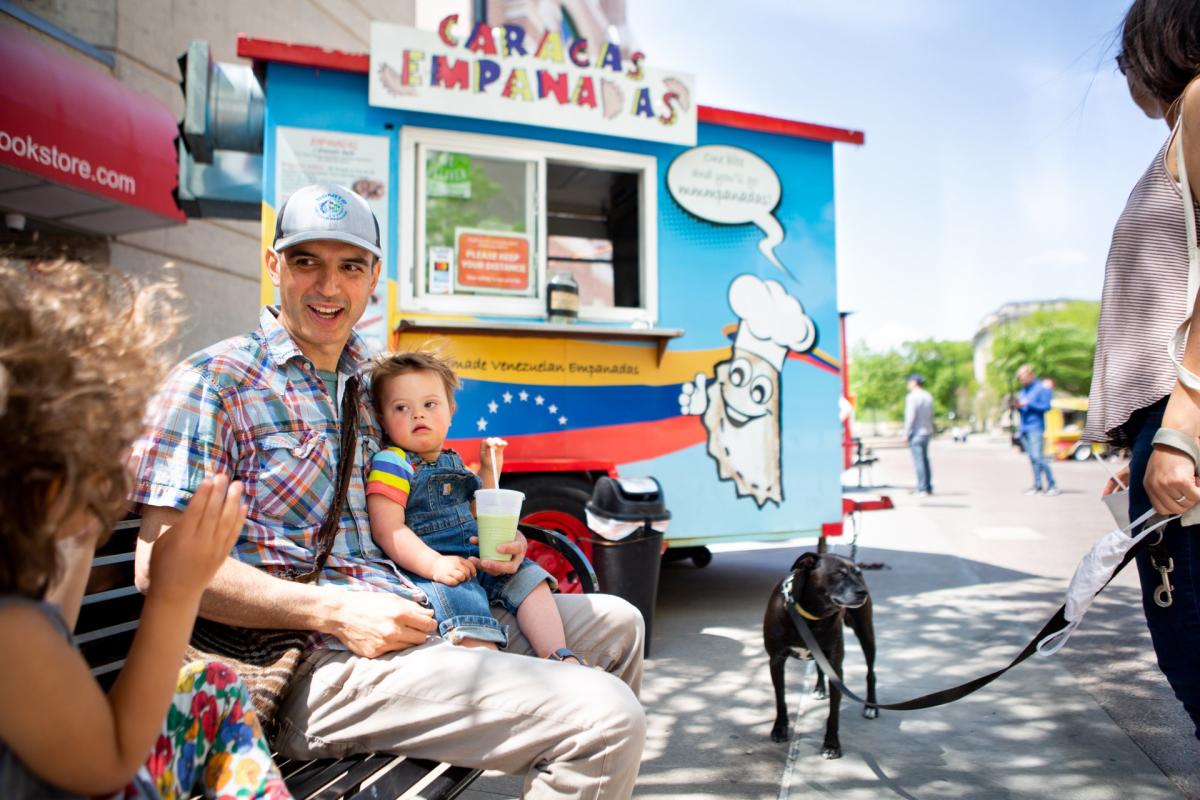 A man and his child sit in front of a food truck parked near the Capitol Square.