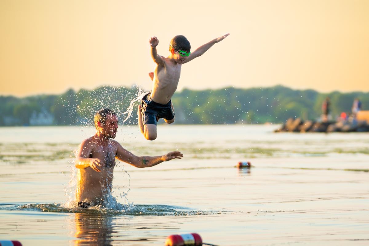 A child jumps off a man's shoulders into the water