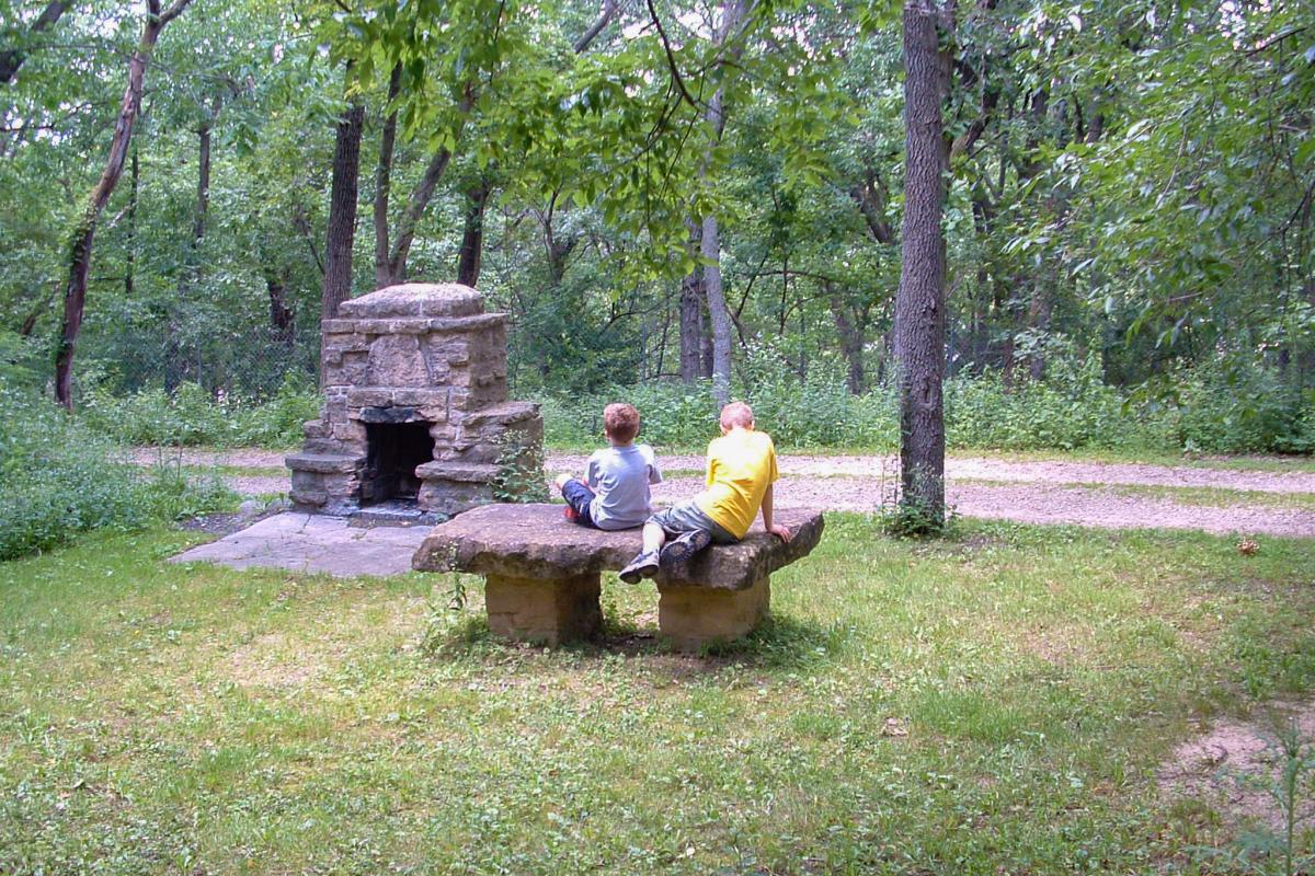 Two children sit on a bench in front of a brick fire pit at Hoyt Park