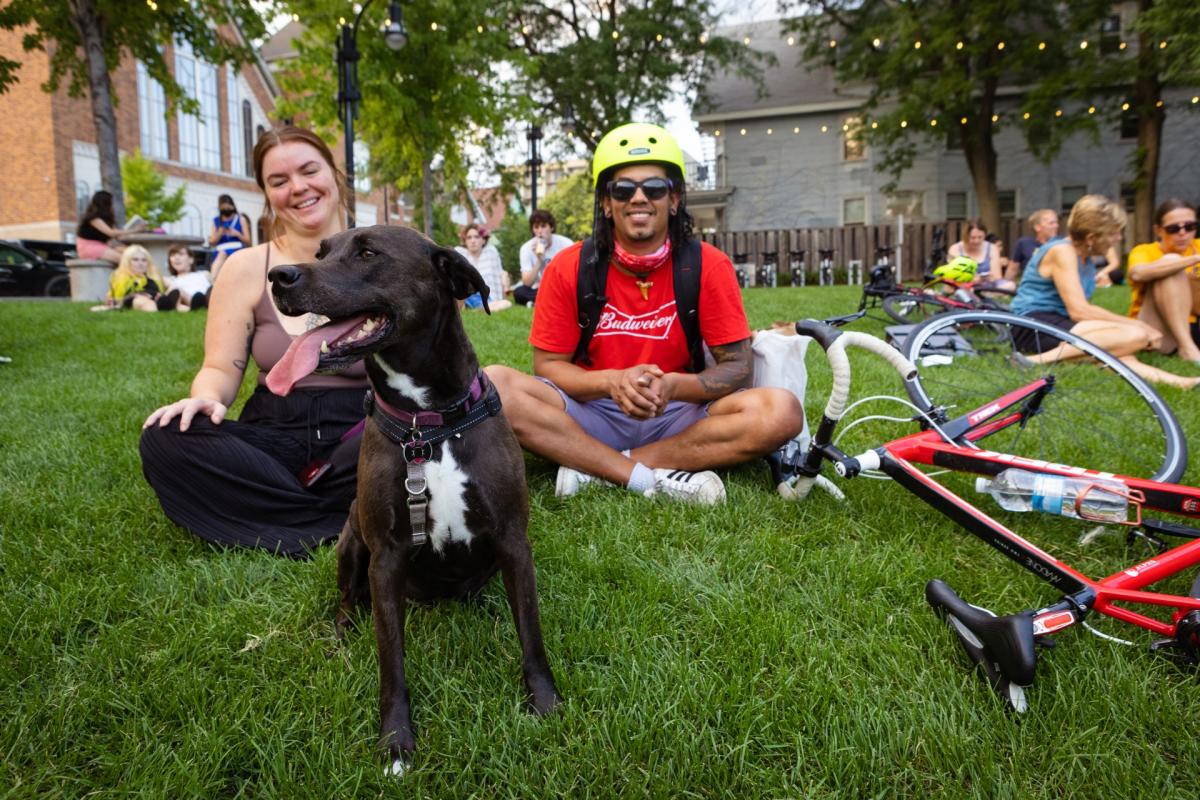 A white woman, Black man, and a dog sit on the ground at Peace Park during a nighttime concert