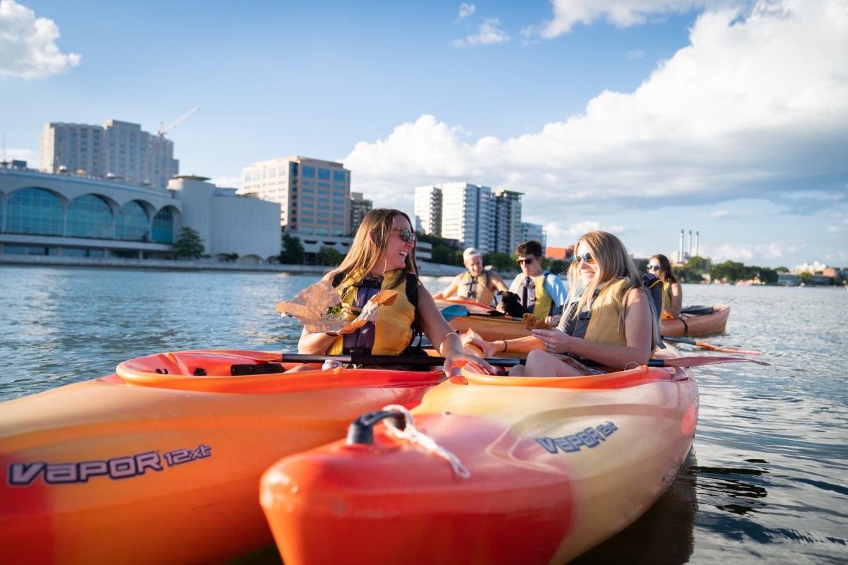 A group of friends enjoy sandwiches while kayaking in front of Monona Terrace on Lake Monona